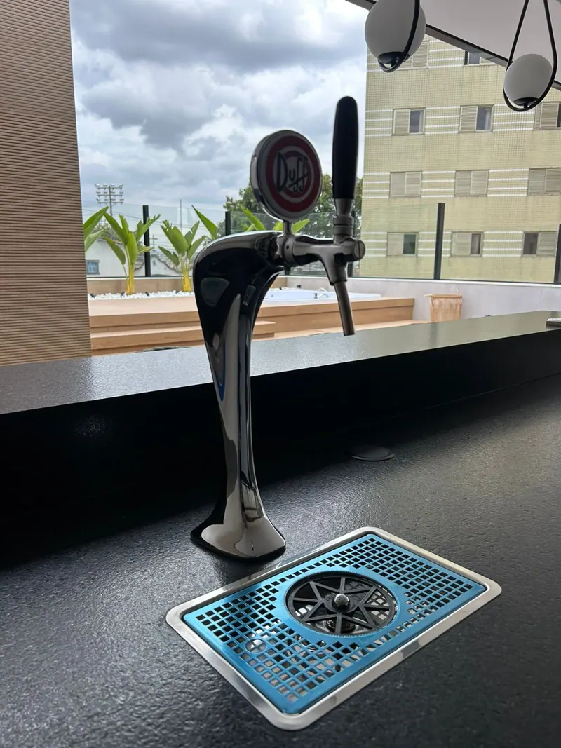 Torre Naja cromada de uma torneira num balcão preto, com bandeja de embutir de grelha azul